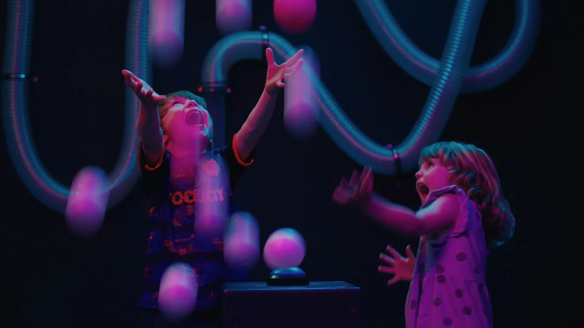 Visitors feeding coloured balls into transparent pneumatic tubes in the Scatter installation